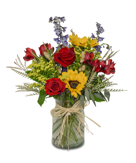Vibrant bouquet of sunflowers, blue delphinium, red roses, and spray chrysanthemums in a clear glass vase.