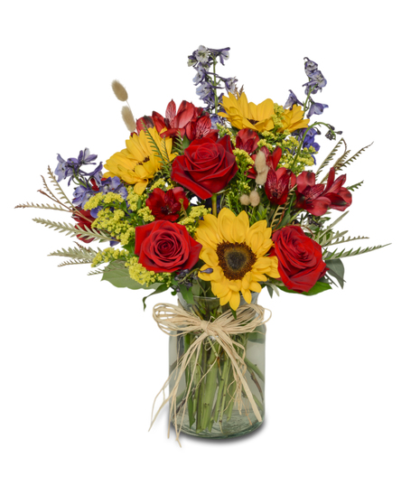 Vibrant bouquet of sunflowers, blue delphinium, red roses, and spray chrysanthemums in a clear glass vase.