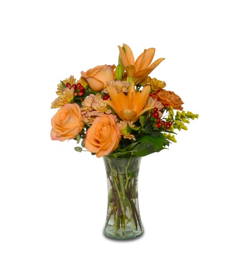 Clear vase filled with orange lilies, tangerine roses, peach daisy mums, orange mini roses, yellow solidago,  and red hypericum berries.