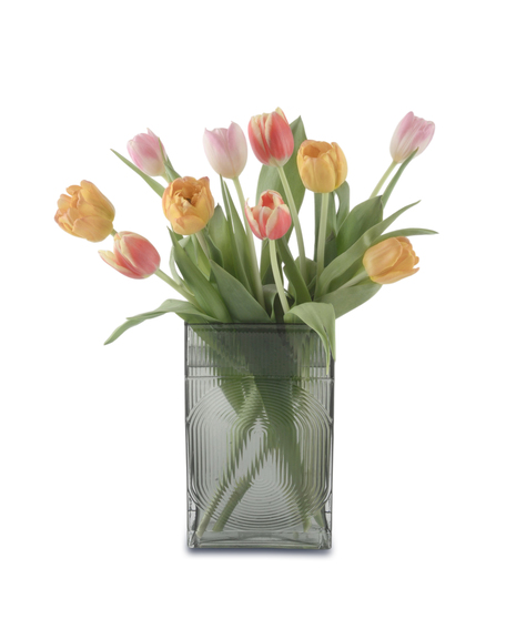 Colorful tulip arrangement in a textured glass vase featuring pink, coral, and yellow blooms with green foliage, styled in a loose, airy spring design.