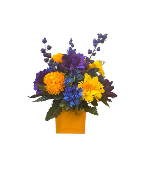 A cube vase filled with a mix of colorful, lifelike faux flowers including zinnias, ferns, and other blooms. Designer’s choice; styles will vary.