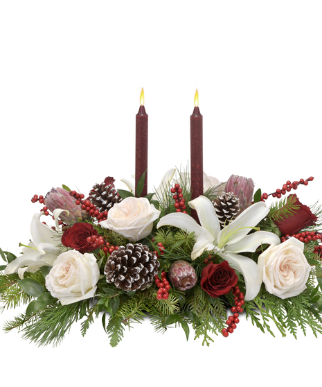 Luxurious centerpiece with garden roses, mink proteas, white lilies, Italian ruscus, pine, berries, frosted pinecones, and candles. A festive sensory delight.