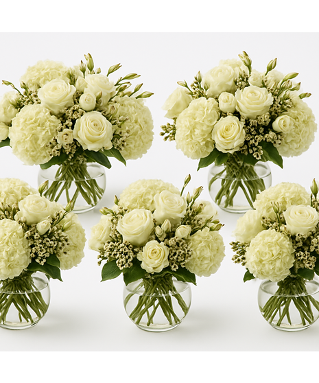 A luxurious floral arrangement of ivory roses, white hydrangeas, and lisianthus, set in a clear vase with lush greenery accents.