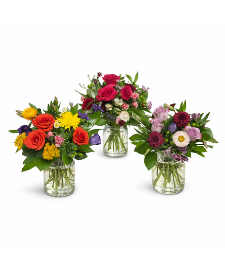 Seasonal mixed flower arrangement with three roses and fresh accent blooms in a 5-inch clear glass cylinder vase with lemon leaf greenery.