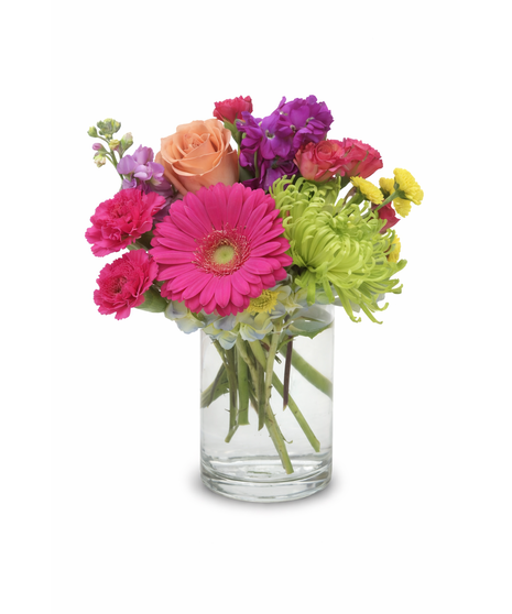 Bright mixed flower arrangement with hot pink, yellow, and orange gerbera daisies, roses, mums, and carnations in a clear glass cylinder vase.