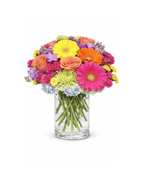 Bright mixed flower arrangement with hot pink, yellow, and orange gerbera daisies, roses, mums, and carnations in a clear glass cylinder vase.