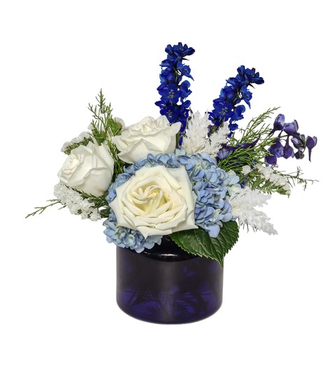 Blue and white winter floral arrangement with hydrangeas, delphinium, white roses, and frosty white pampas in a cool, elegant design.