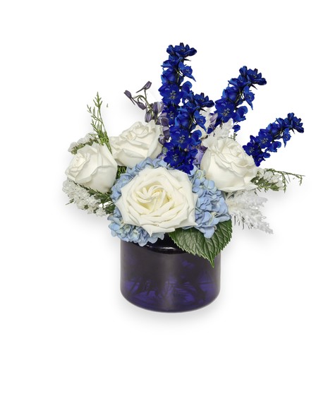 Blue and white winter floral arrangement with hydrangeas, delphinium, white roses, and frosty white pampas in a cool, elegant design.