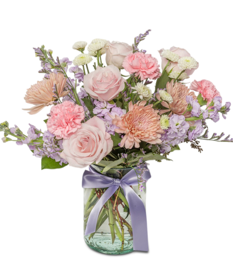 Amelia is a pastel bouquet with pink roses, lavender stock, Linette mums, and carnations in a clear jar tied with a lavender ribbon. Ideal for Mother's Day and more.