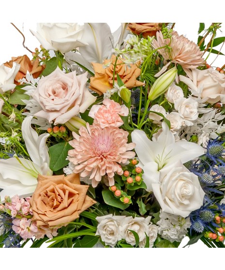Ascent floral arrangement with neutral roses, white lilies, hydrangea, chrysanthemums, eryngium, curly willow, and greenery in a glass vase