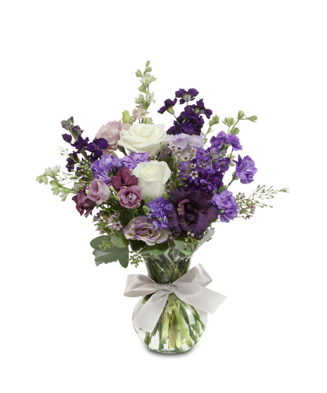 A mix of white roses and purple flowers in a clear glass vase tied with a bow.